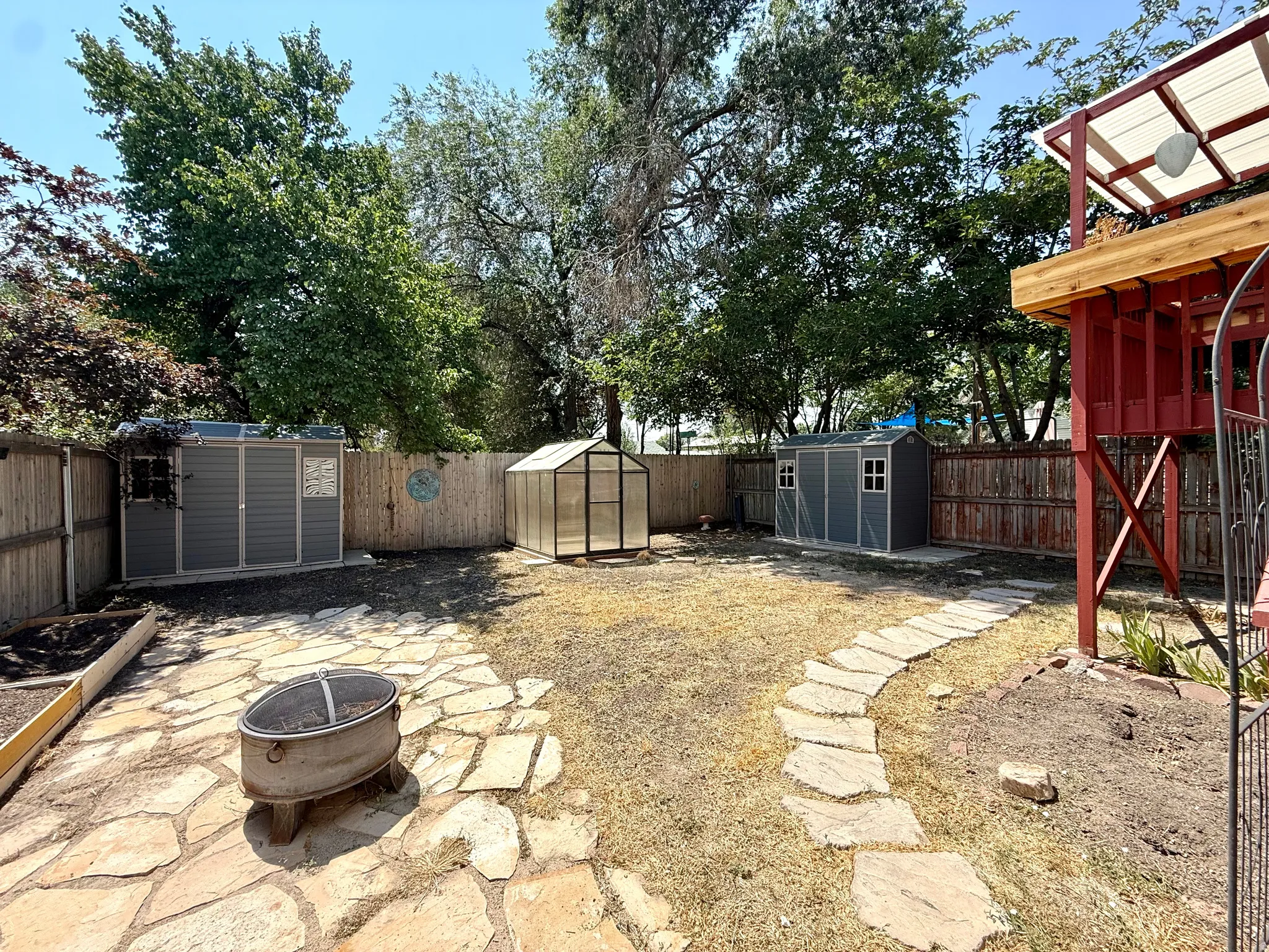 Expansive backyard featuring a stone patio with a built-in fire pit, a stepping stone path, and a raised garden bed