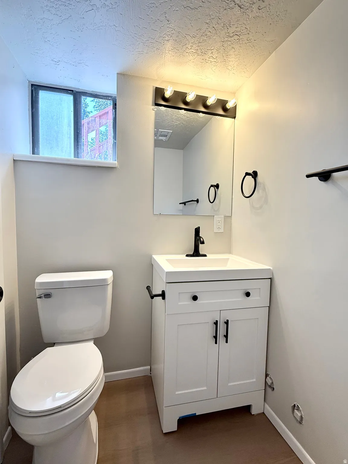 Bathroom featuring a white vanity with black hardware, a black faucet, and a black-framed mirror with multi-bulb lighting