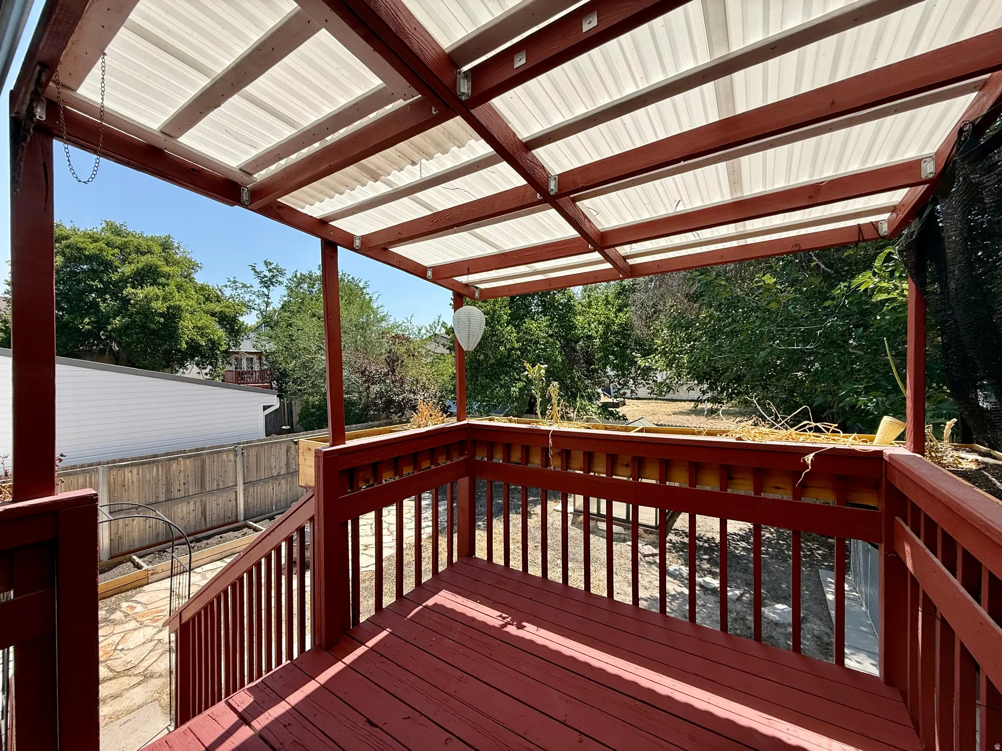 Red-stained wooden deck featuring a slatted railing and a translucent corrugated roof covering