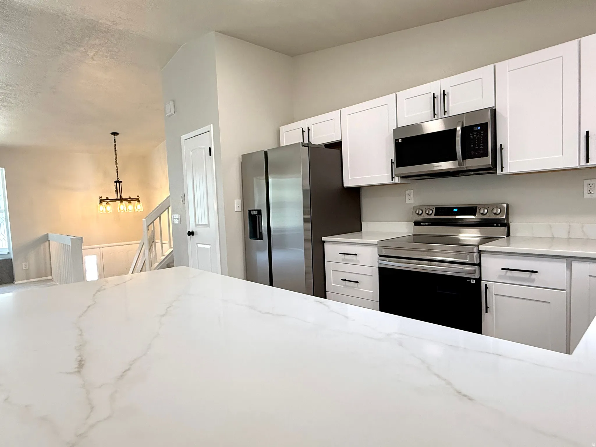 Kitchen featuring white shaker-style cabinetry, stainless steel appliances, and a substantial white countertop with subtle veining