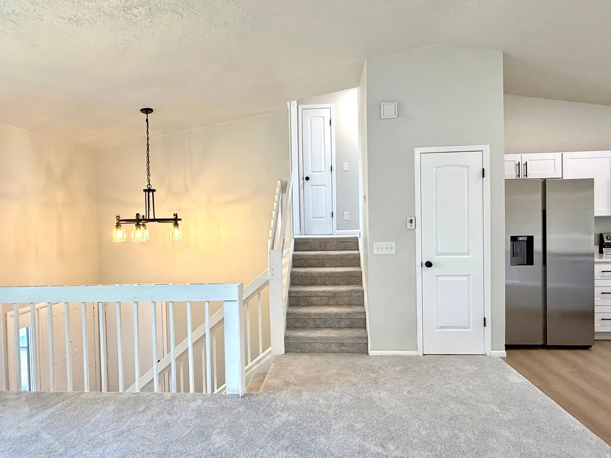 Upper level landing featuring light gray carpeting, white balustrade, and vaulted ceiling