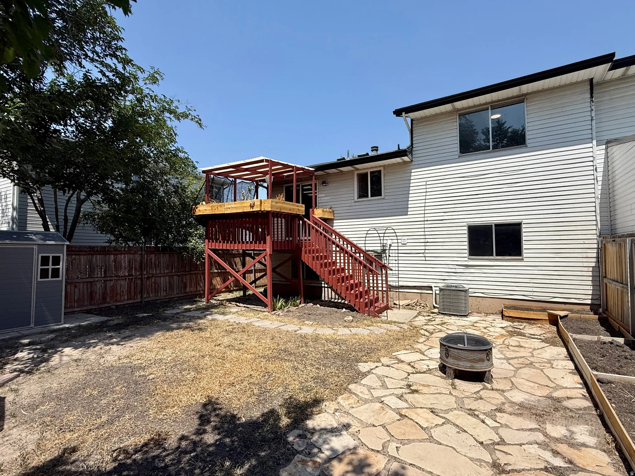 Expansive backyard featuring a multi-level deck with a pergola, flagstone patio, raised garden beds, and a storage shed
