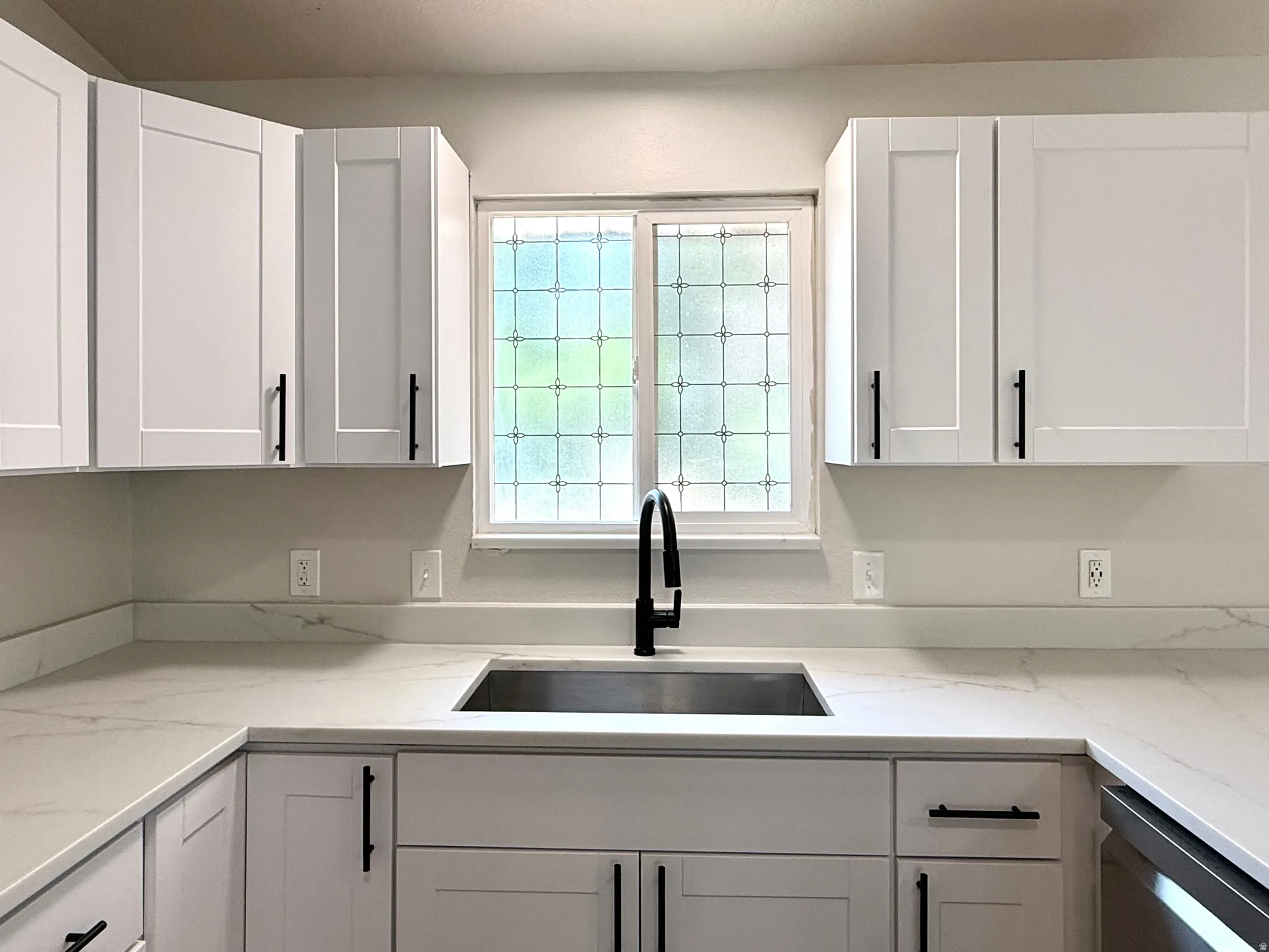 Kitchen featuring white shaker-style cabinetry, a stainless steel undermount sink, a matte black gooseneck faucet, and light-toned countertops with subtle veining