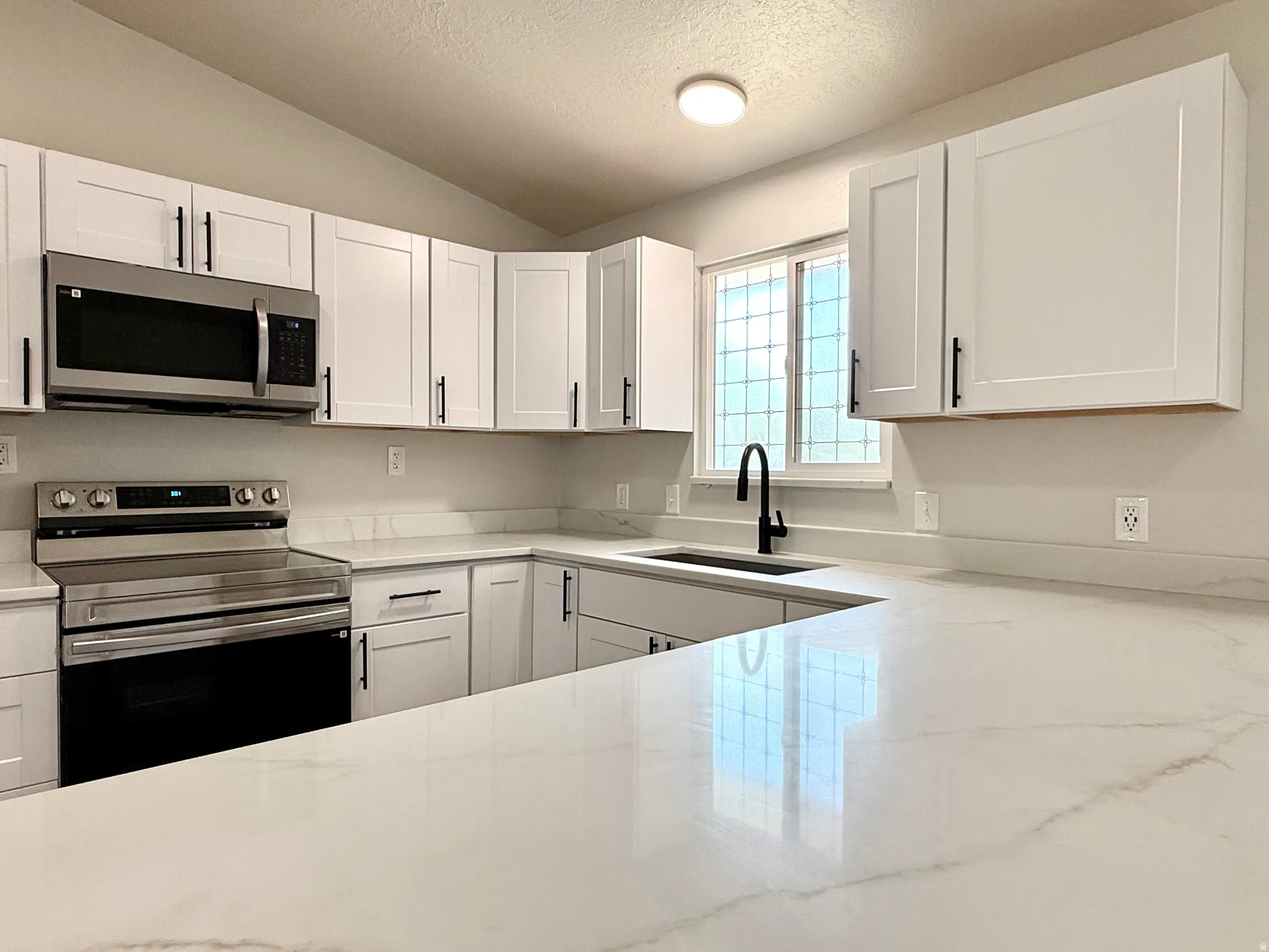 Modern kitchen featuring white shaker cabinetry, stainless steel appliances, a black matte faucet, and white countertops with subtle veining