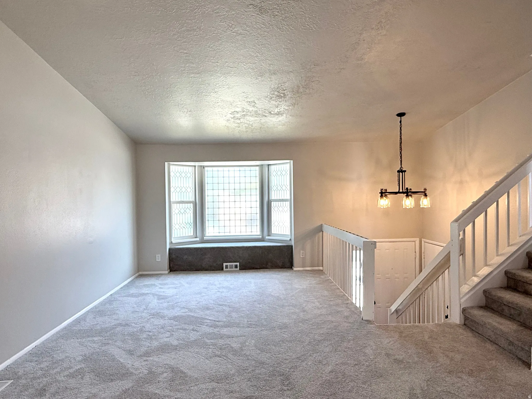 Spacious interior featuring neutral paint, gray carpet, a bay window with decorative glass, and a modern chandelier