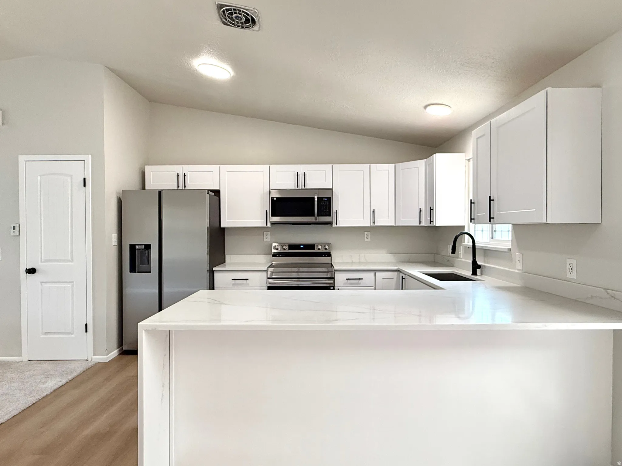 Modern kitchen featuring white shaker cabinetry, stainless steel appliances, a bar-height countertop, a matte black faucet, and wood-finish flooring
