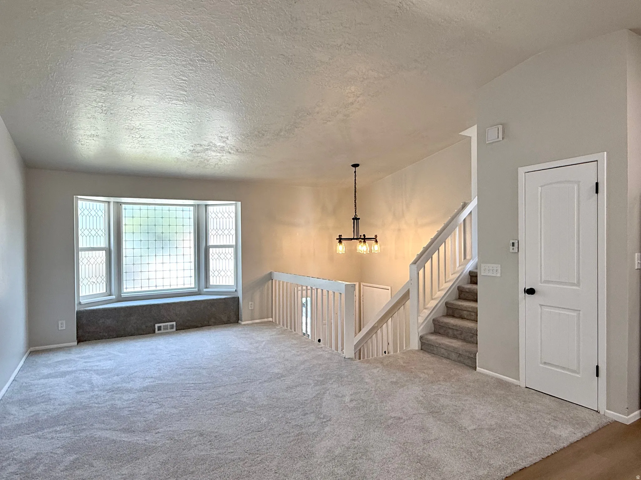 Spacious living area featuring light gray carpet flooring and a prominent bay window with decorative glasswork