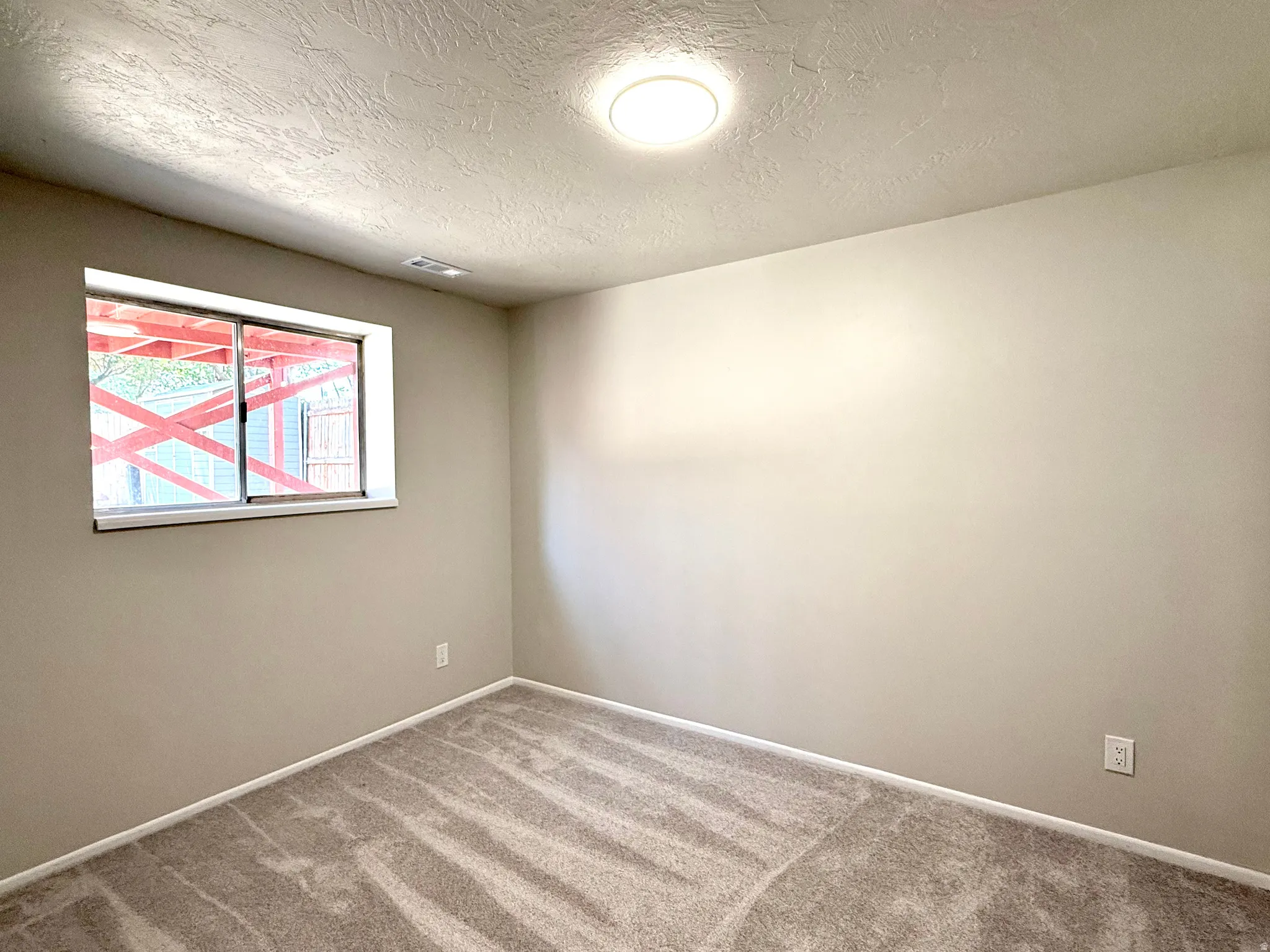 Room featuring a window with a white frame, textured ceiling, flush-mount ceiling light, light-toned walls, and patterned carpeting