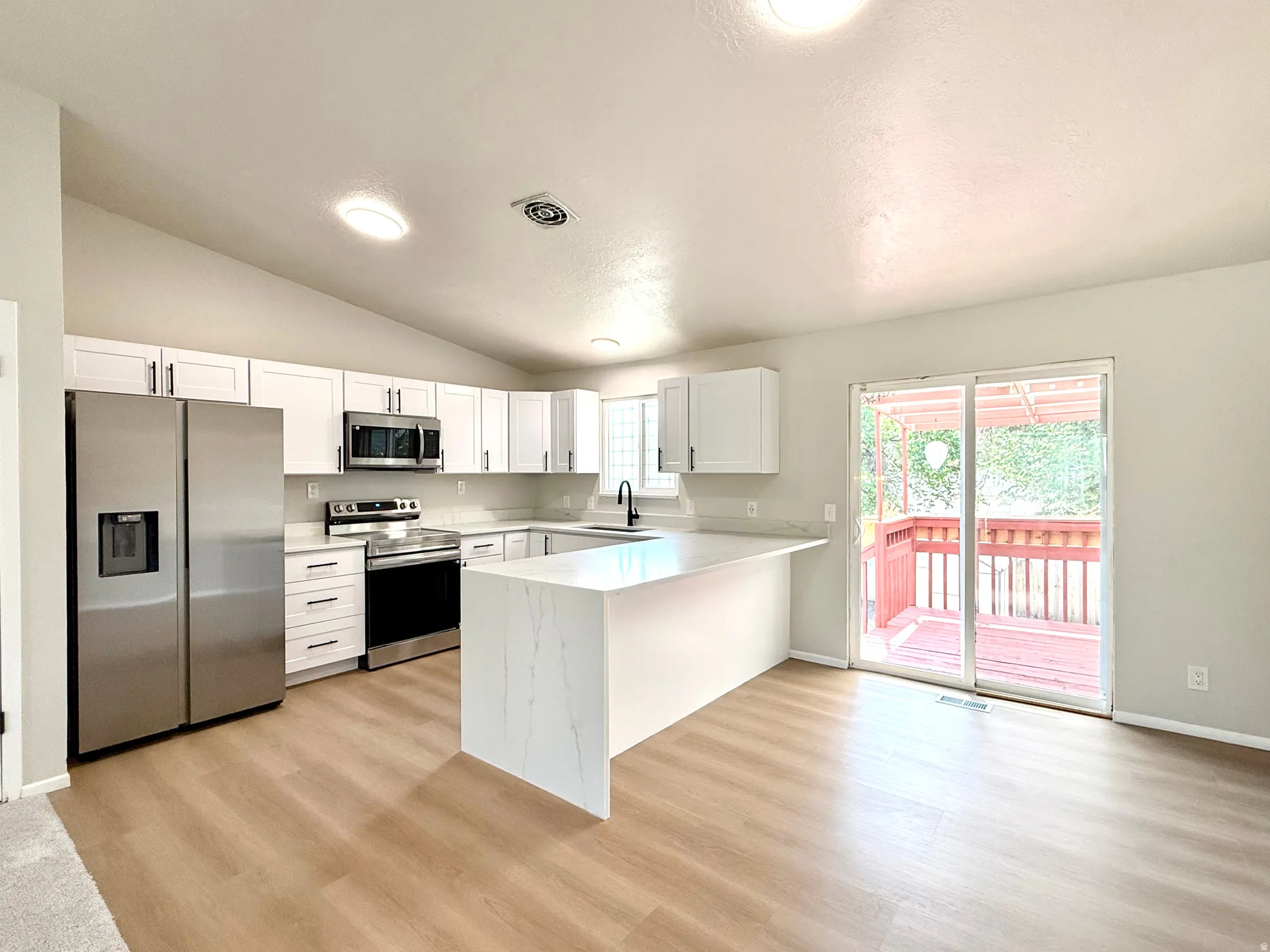 Contemporary kitchen featuring white cabinetry, stainless steel appliances, a white waterfall island, and wood-finish flooring