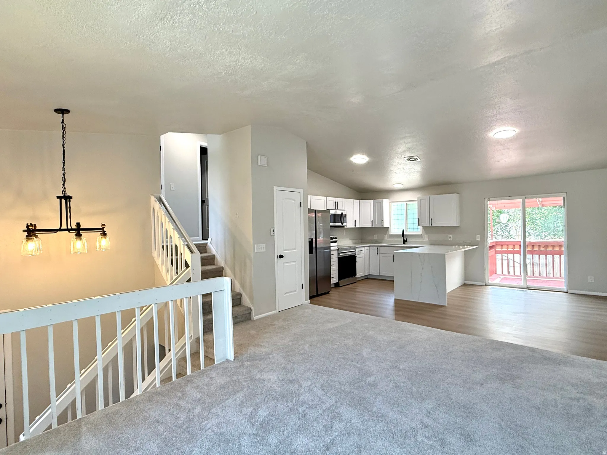 Open-concept living area with vaulted ceilings, contemporary kitchen with white cabinetry, stainless steel appliances, and a central island with a waterfall countertop