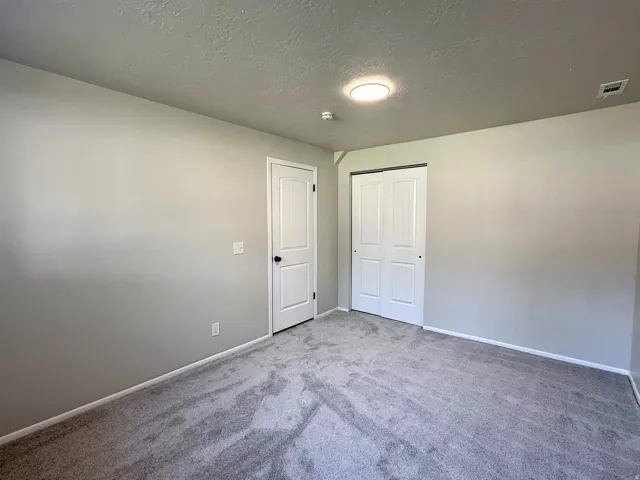 Bedroom featuring light gray wall paint, gray carpet flooring, white baseboards, and a white paneled door with black hardware