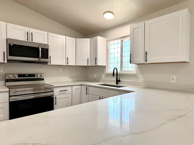 Modern kitchen featuring white shaker cabinetry, stainless steel appliances, a black matte faucet, and white countertops with subtle veining