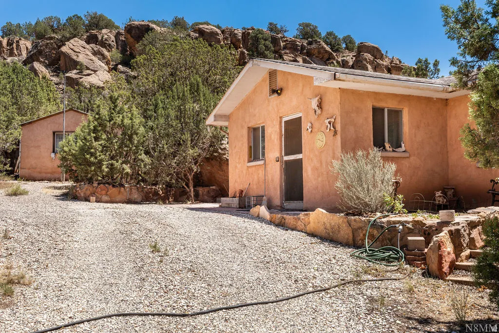 Adobe-style exterior with a gravel driveway, featuring a secondary detached structure and a rock retaining wall