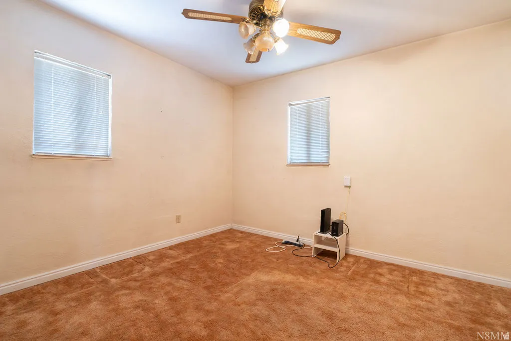 Carpeted room featuring a ceiling fan with light fixture and two windows with blinds