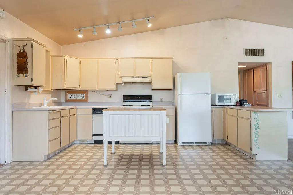Kitchen featuring vaulted ceilings, track lighting, ample cabinetry, a freestanding range, and a dishwasher