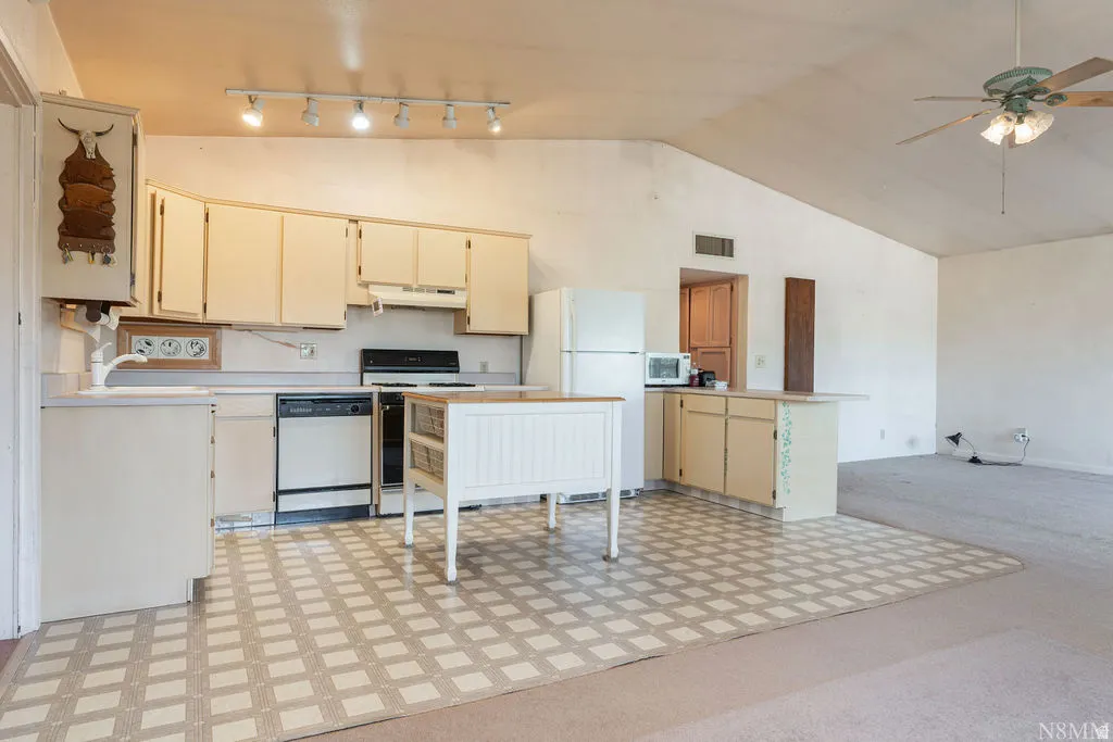 Spacious open-concept kitchen and living area featuring cream-toned cabinetry, stainless steel range, geometric patterned tile flooring, track lighting, and ceiling fan