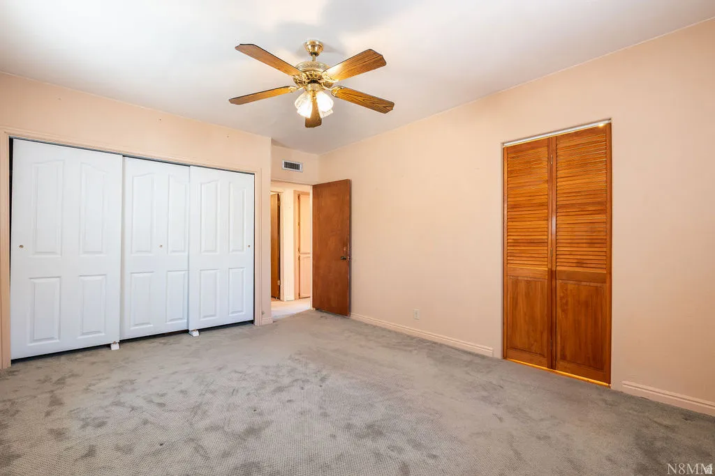 Room featuring neutral-toned walls, carpet flooring, and a ceiling fan with light fixture