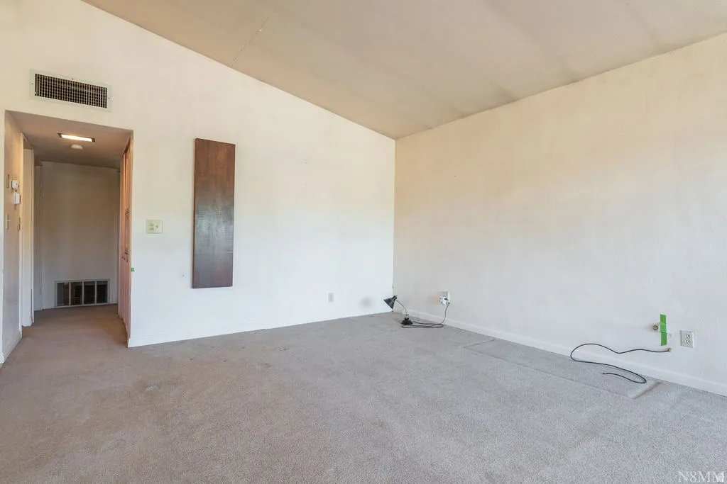 Spacious living area with neutral carpet flooring, fresh white walls, and abundant natural light from recessed ceiling fixtures