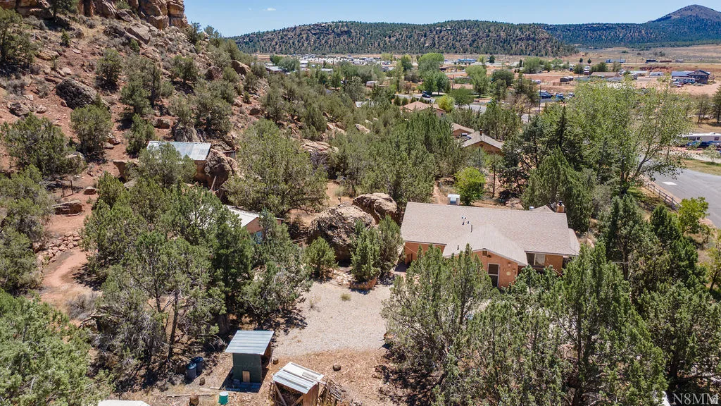 Expansive property featuring a single-story residence with a brown shingle roof, surrounding mature trees, and natural rock formations