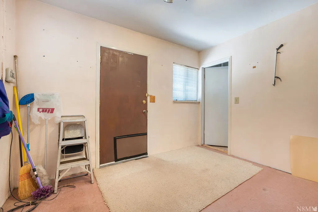 Utility room featuring concrete flooring, metal step ladder, and direct access to exterior door with transom window for natural light