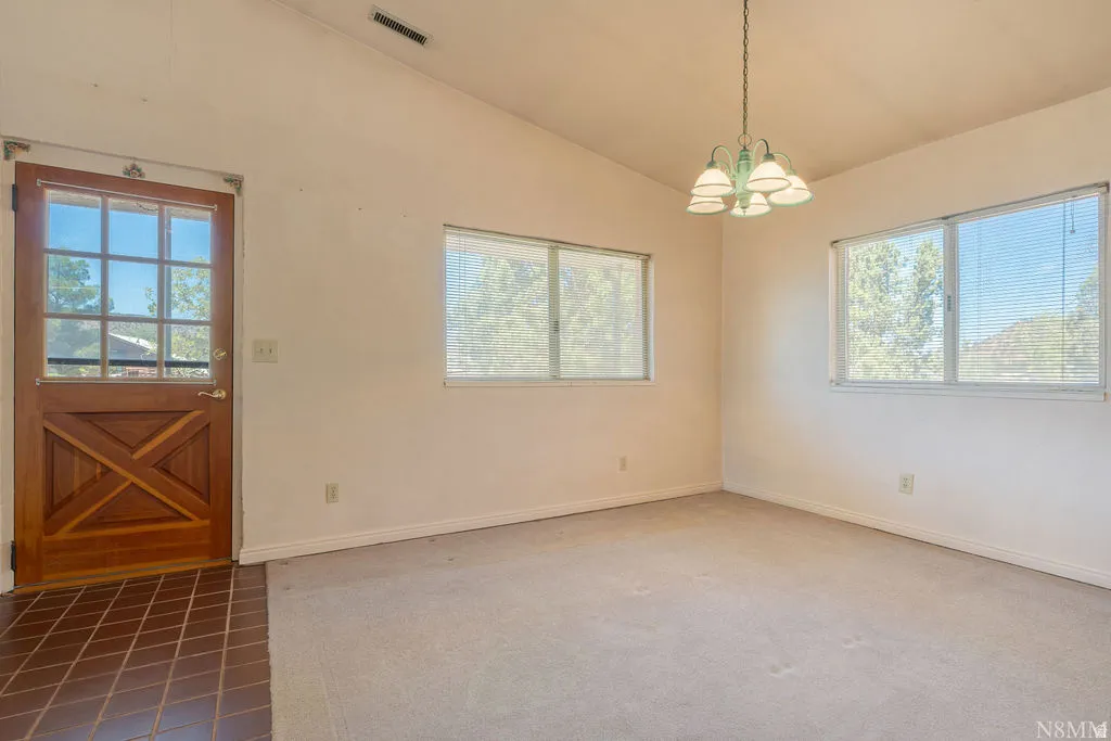 Room with vaulted ceiling, light-colored carpet, and multiple windows