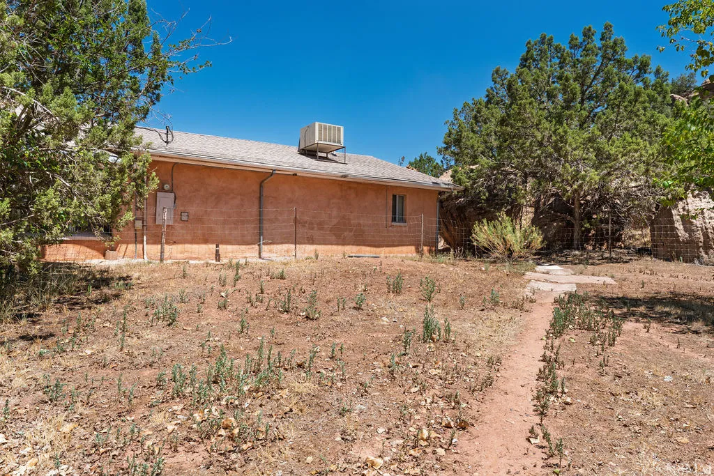 Brick residential structure with a flat roof and rooftop HVAC unit, situated on a spacious desert lot surrounded by mature native vegetation and natural landscaping
