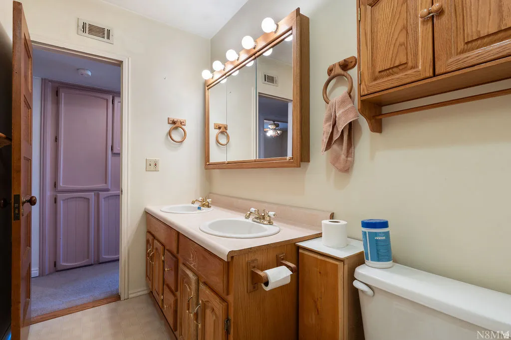 Elegant primary bathroom featuring warm wood cabinetry with ample storage, a ceramic pedestal sink, and brass hardware