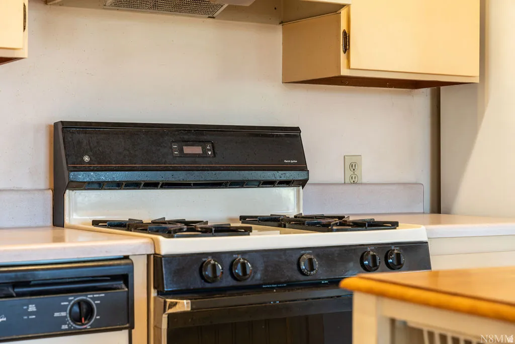 Kitchen featuring a gas range, dishwasher, light-colored countertops, and upper cabinetry