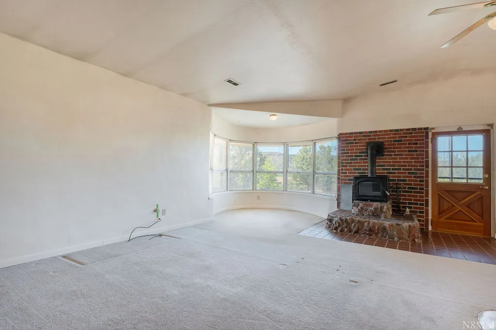 Living space featuring a prominent wood-burning stove with a brick and stone hearth, a curved bay window, and a wood door with a grid window