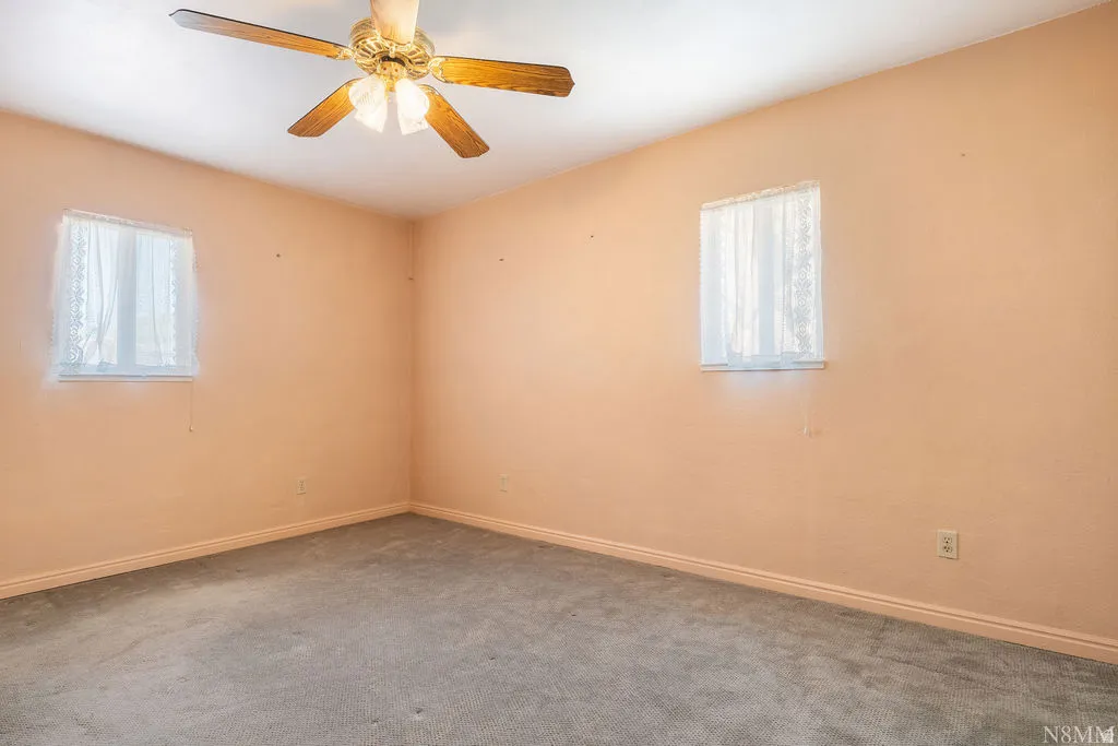 Ceiling fan with light fixture, two windows, wall-to-wall carpeting, and baseboard trim