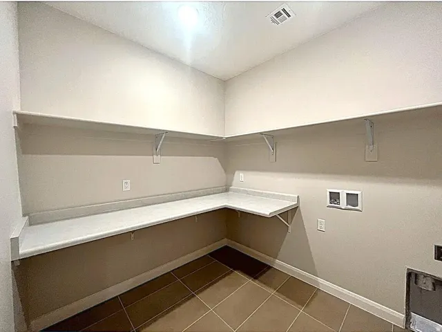 Utility room featuring extensive built-in shelving, a corner countertop with a backsplash, and tile flooring