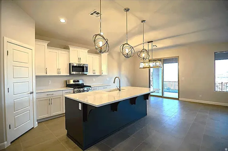 Kitchen featuring a large island with a light-toned countertop, white cabinetry, stainless steel appliances, and a gas range