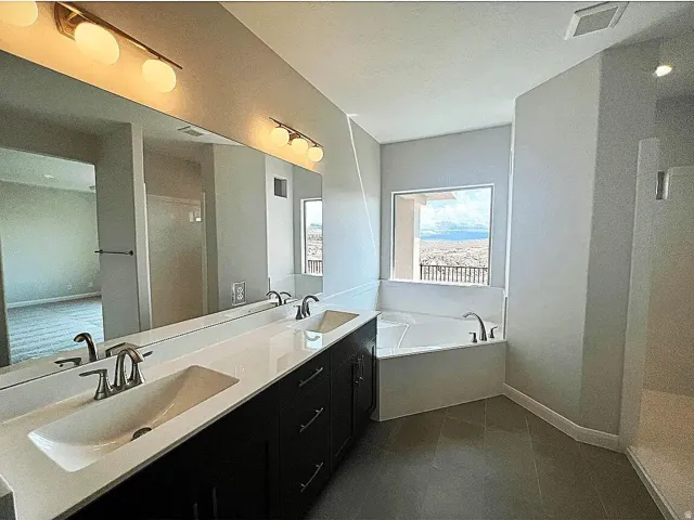 Bathroom featuring a dual vanity with undermount sinks, a built-in soaking tub, a separate shower enclosure, and tiled flooring