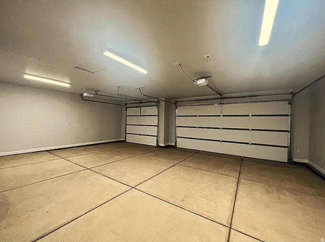Two-car garage featuring a concrete floor, two white paneled garage doors, overhead fluorescent lighting, and painted walls