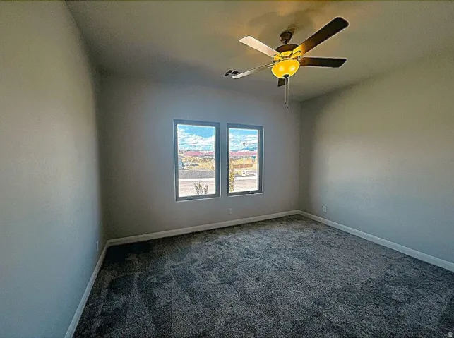 Spacious room featuring neutral-toned walls, dark patterned carpeting, and a ceiling fan with integrated lighting