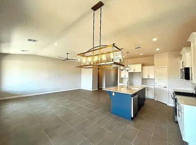 Open-concept living space featuring a spacious kitchen with a blue island, white cabinetry, and stainless steel appliances
