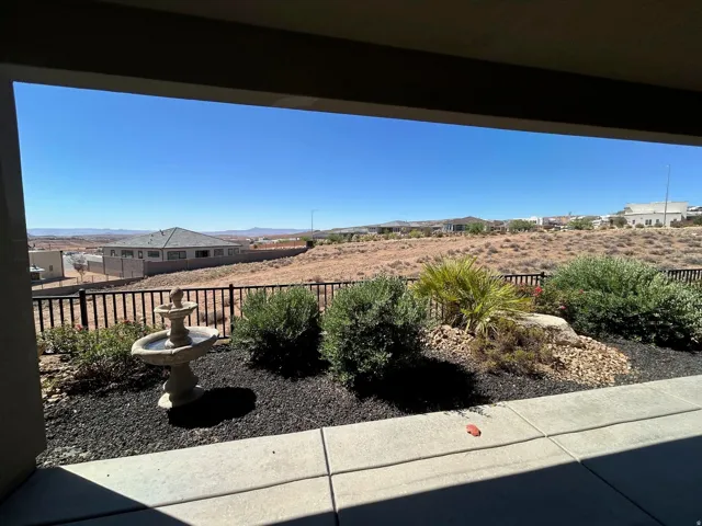 Covered patio with concrete flooring, featuring a decorative tiered fountain, established landscaping with various shrubs and rock elements, and black mulch