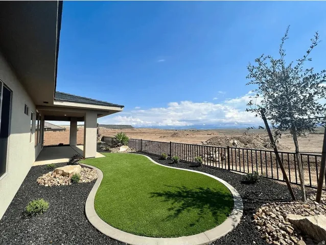 Expansive backyard oasis featuring a curved, professionally manicured lawn with concrete edging, decorative rock landscaping, and black metal railing that borders the entertaining space
