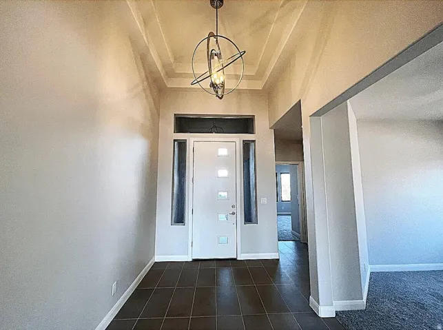 Welcoming foyer featuring dark tile flooring, white painted walls, and a modern orbital pendant light fixture