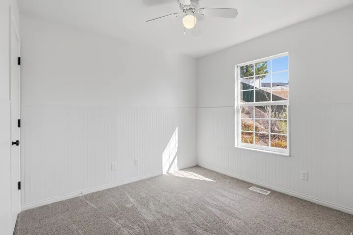 Bright room featuring a window with grid panes, white vertical wainscoting, and gray carpeting