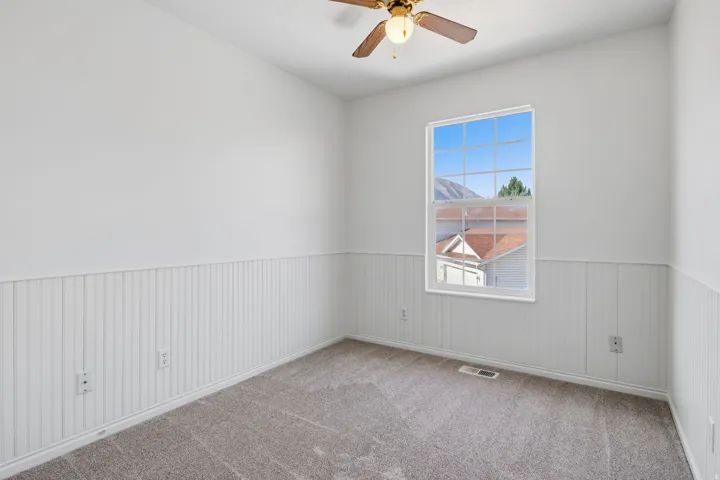 Room featuring white beadboard wainscoting, light gray carpet flooring, and a ceiling fan with integrated lighting