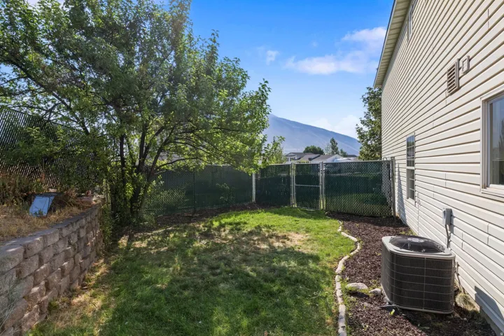 Private backyard featuring a mature shade tree, a stone retaining wall, and green chain-link fencing
