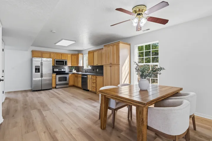 Open-concept living space featuring wood-finish flooring, a kitchen with stainless steel appliances, light wood cabinetry, and a ceiling fan with integrated lighting