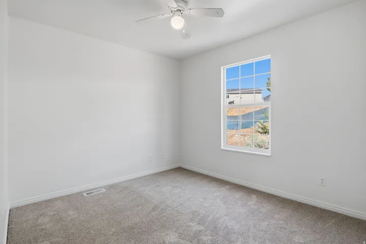 Bright bedroom featuring neutral carpet flooring, ceiling fan with integrated lighting, and a large double-hung window framing natural light and scenic vistas