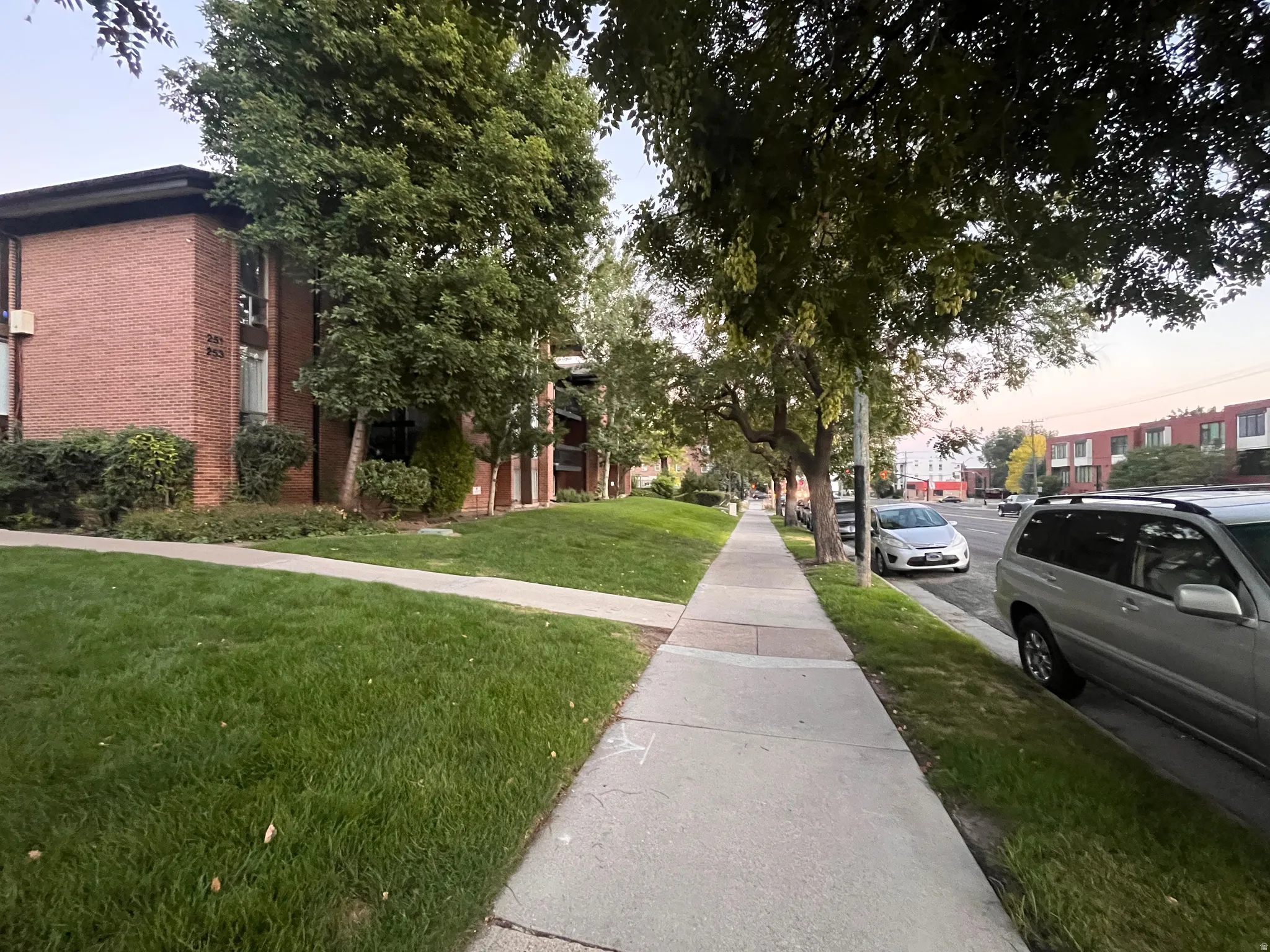 Brick facade building with multiple windows, surrounded by mature trees and a manicured lawn