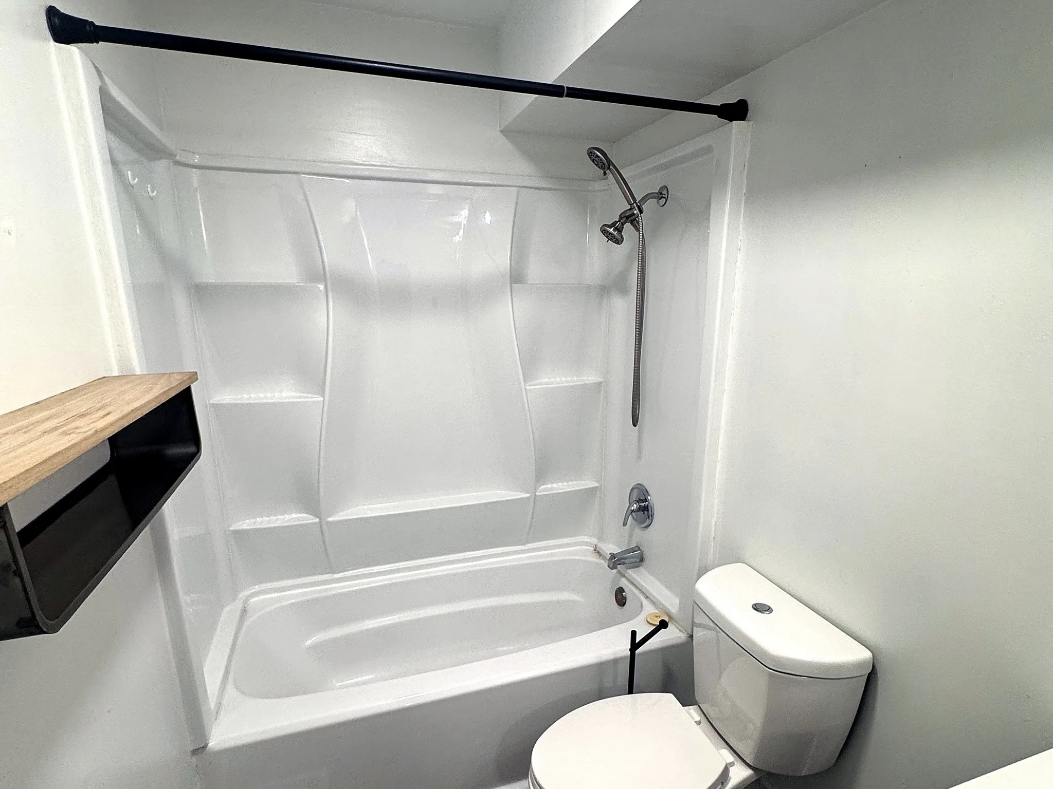 Bathroom featuring a white tub and shower combination with integrated shelving, a chrome shower head, and a white toilet