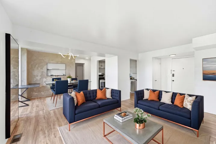 Open-concept living space with wood-finish flooring, a contemporary linear chandelier, and a textured accent wall