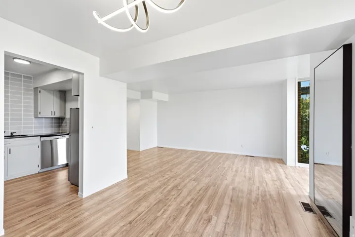 Open-concept living space featuring wood-finish flooring, a modern overhead light fixture, and abundant natural light