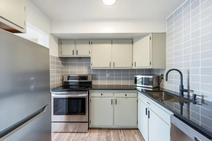 Kitchen featuring light-toned cabinetry, a black countertop, a stainless steel electric range, a stainless steel refrigerator, and a stainless steel dishwasher