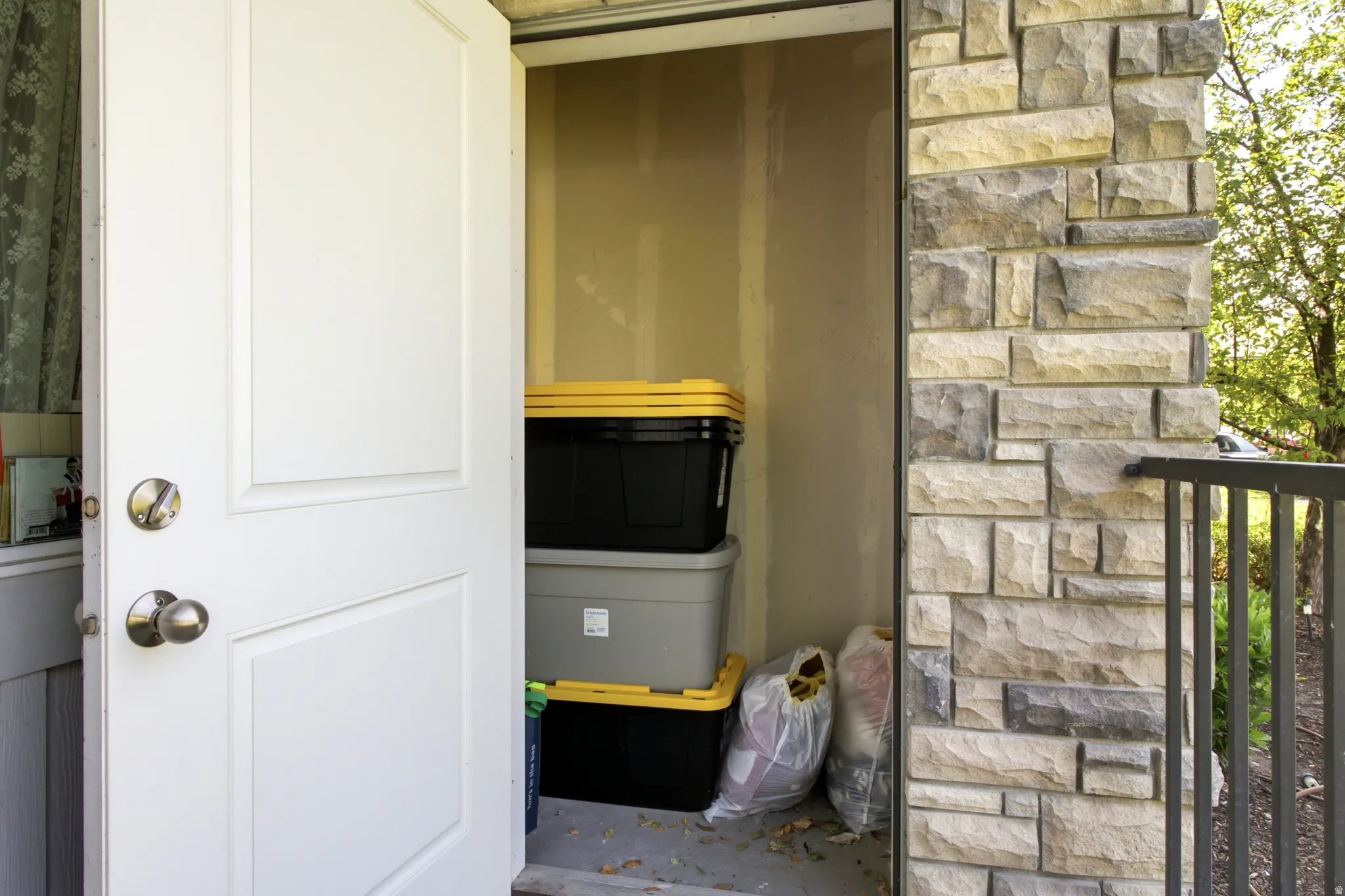Exterior storage nook with a paneled door, stone facade, and metal railing
